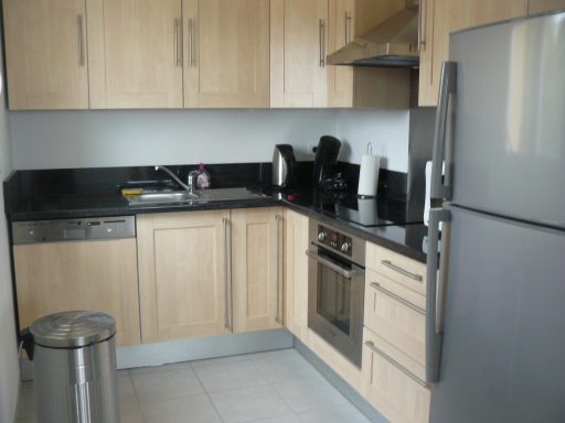 Cuisine moderne avec meubles en bois clair, plan de travail noir, et électroménagers en acier.